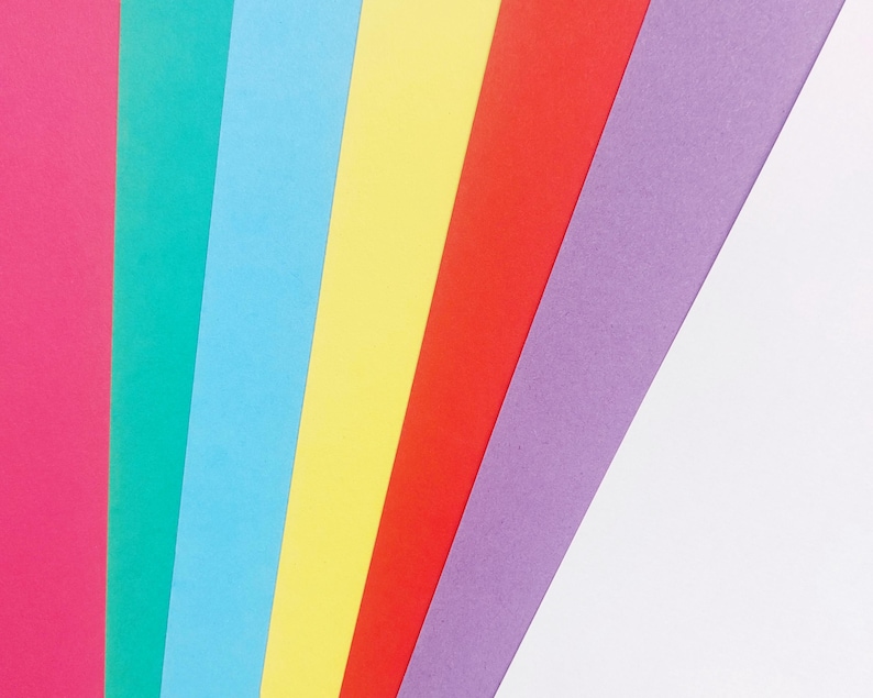 May include: A rainbow of colored paper strips arranged in a diagonal pattern. The colors are pink, teal, light blue, yellow, red, purple, and white.