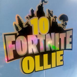 May include: A black and yellow Fortnite cake topper with the number 10 and the name Ollie. The topper is made of iridescent material.