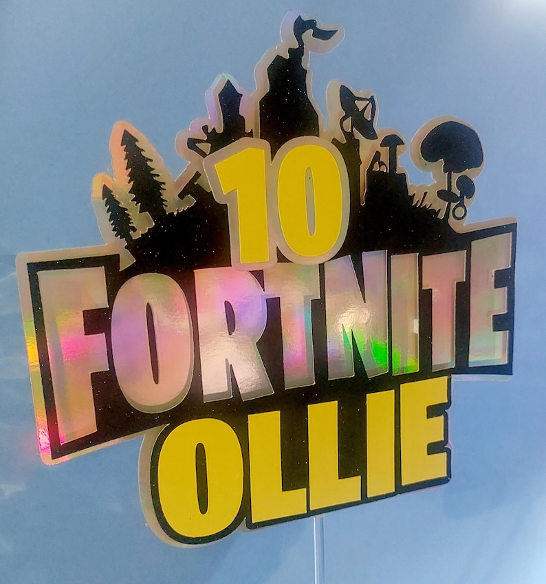 May include: A black and yellow Fortnite cake topper with the number 10 and the name Ollie. The topper is made of iridescent material.
