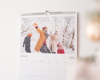 Op de afbeelding: Een kalender met een foto van een gezin dat in de sneeuw speelt. De maand is januari 2025. De foto toont een gezin van vier, waaronder twee kinderen, die in een besneeuwd bos spelen.