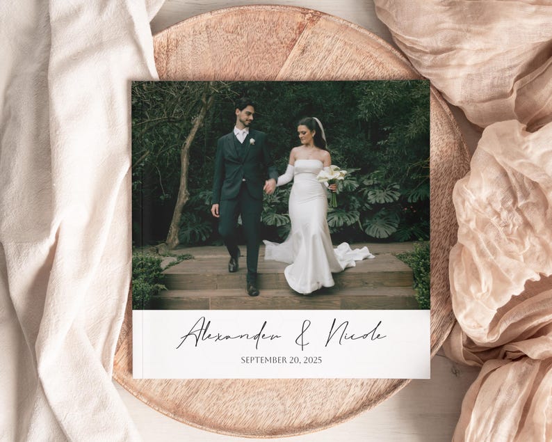 Pode incluir: Um &aacute;lbum de fotos de casamento com um casal de m&atilde;os dadas num jardim. A capa exibe os nomes "Alexander & Nicole" e a data "September 20, 2025" em escrita cursiva. O &aacute;lbum est&aacute; sobre uma bandeja decorativa.