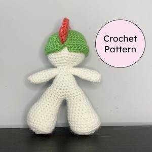 May include: A handmade crochet doll with a white body, green head, and red spike. The doll has outstretched arms and wide legs. The image includes a pink circle with the words "Crochet Pattern".