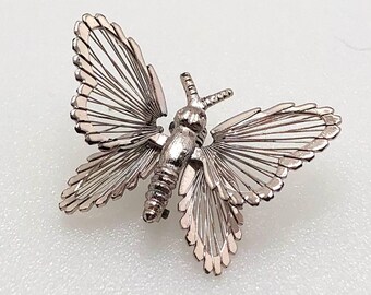 May include: A silver butterfly brooch with delicate wire wings. The wings are made of thin, silver wire that is arranged in a radial pattern. The butterfly's body is also made of silver and has a detailed design.