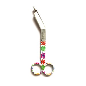 Könnte beinhalten: Eine weiße Bandagenschere mit Blumenmuster. Die Schere hat eine gebogene Klinge und wird von Panther Surgical hergestellt.