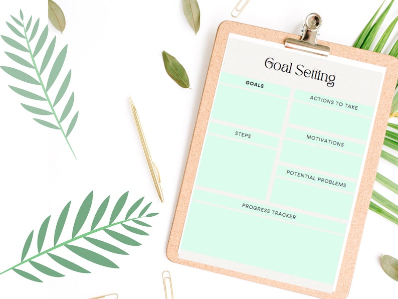 May include: A printable goal setting worksheet with sections for goals, actions to take, steps, motivations, potential problems, and a progress tracker. The worksheet is on a corkboard with a green plant in the background.