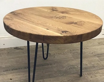 May include: Round wooden coffee table with a natural wood finish and black hairpin legs. The table is sitting on a wood floor with a patterned design.