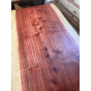 Könnte beinhalten: Nahaufnahme einer großen Holzplatte mit einem rötlich-braunen Farbton. Das Holz hat eine natürliche Maserung und mehrere Knoten. Die Oberfläche ist glatt und poliert.