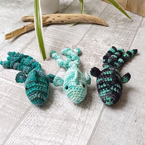 May include: Three crocheted fish toys in shades of green and black. The fish are lying on a white wooden surface.