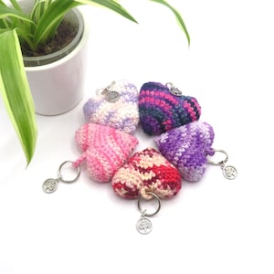 May include: Five crocheted heart-shaped keychains in pink, purple, and white with silver key rings and charms. Each charm features a tree design.