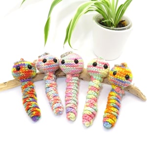 May include: Five colourful crocheted worm keyrings with black eyes. The worms are made with a variety of bright colours, including pink, yellow, orange, and green.