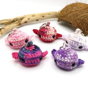 May include: Five crocheted dolphin keychains in various shades of pink, purple, and white. Each keychain has black eyes and a silver key ring.