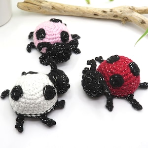 May include: Three crocheted ladybugs in pink, red, and white with black spots and legs.