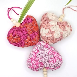 May include: Three crocheted hearts in pink, red, and white with wooden beads hanging from each.