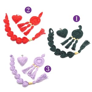 Könnte beinhalten: Drei Sätze gehäkelter herzförmiger Ornamente mit Quasten und Perlen. Die Sätze sind in Rot, Grün und Lila.
