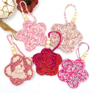 Peut inclure: Cinq ornements en forme d'étoile en crochet avec des perles en bois. Les ornements sont dans des tons de rose, rouge et blanc.