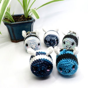May include: Five crocheted bee keychains in blue and white. The bees have black stripes and cute faces.