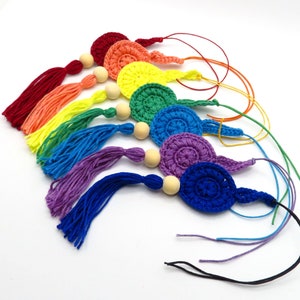 Könnte beinhalten: Ein Set aus sieben gehäkelten regenbogenfarbenen Kreisen mit Holzperlen und Quasten. Die Kreise sind in den Farben des Regenbogens, beginnend mit Rot und endend mit Lila. Jeder Kreis hat eine kleine Holzperle daran befestigt, und eine Quaste hängt an der Unterseite jedes Kreises.