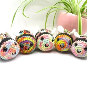 May include: Five crocheted bee keychains with colorful stripes and black accents. Each bee has a white crocheted wing and black button eyes.
