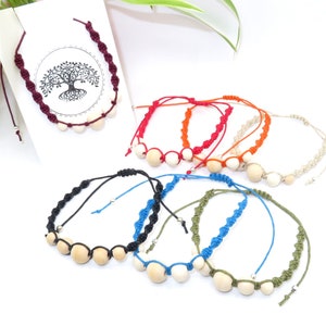 Op de afbeelding: Assortiment van kleurrijke armbanden met houten kralen. Elke armband is gemaakt met een andere kleur touw en heeft een eenvoudig knoopontwerp. De armbanden zijn in een halve cirkel op een witte achtergrond gerangschikt.