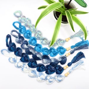 Op de afbeelding: Vijf gehäkelde hartvormige bladwijzers in tinten blauw, turquoise en wit met houten kralen en kwastjes.