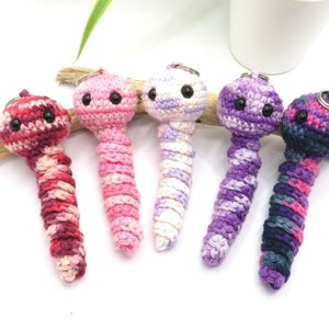 Peut inclure: Cinq porte-clés en forme de vers crochetés dans différentes couleurs, dont le rose, le violet et le bleu. Chaque ver a des yeux noirs et un motif rayé.