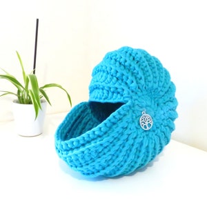Peut inclure: Un panier en crochet bleu turquoise avec un charme en forme d'arbre de vie. Le panier est en forme de demi-sphère et a une large ouverture.