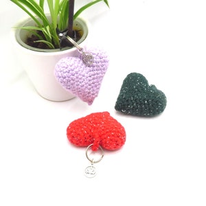 Op de afbeelding: Drie gehaakte hartvormige sleutelhangers in paars, groen en rood. De paarse sleutelhanger heeft een zilveren bedel.
