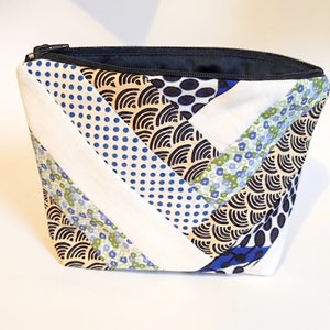 Puede incluir: Un neceser acolchado con cremallera negra e interior azul marino. La bolsa presenta un dise&ntilde;o de patchwork con tela estampada blanca, azul y beige. Los estampados incluyen lunares, flores y dise&ntilde;os ondulados.