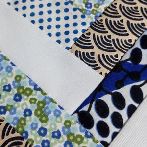 Puede incluir: Primer plano de un patchwork de tela con varios patrones. El dise&ntilde;o incluye telas blancas, azules y beige con lunares, florales y patrones de ondas abstractas. Una banda el&aacute;stica blanca cruza la imagen en diagonal.