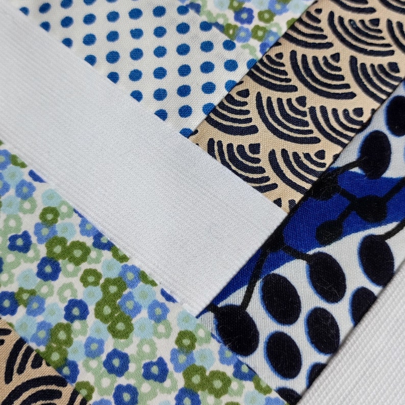 Puede incluir: Primer plano de un patchwork de tela con varios patrones. El dise&ntilde;o incluye telas blancas, azules y beige con lunares, florales y patrones de ondas abstractas. Una banda el&aacute;stica blanca cruza la imagen en diagonal.