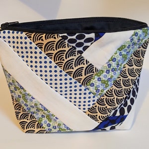 Puede incluir: Un neceser acolchado con cremallera negra. La bolsa presenta un dise&ntilde;o de patchwork con tela estampada blanca, azul y beige. El interior es azul marino.