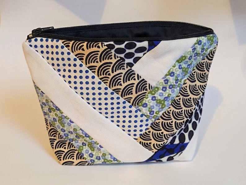 Puede incluir: Un neceser acolchado con cremallera negra. La bolsa presenta un dise&ntilde;o de patchwork con tela estampada blanca, azul y beige. El interior es azul marino.