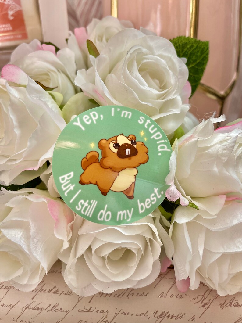 Puede incluir: Una pegatina redonda con una ilustraci&oacute;n de castor de dibujos animados en tonos marr&oacute;n y crema, sobre un fondo verde claro. El texto dice: "Yep, I'm stupid. But I still do my best." La pegatina est&aacute; rodeada de rosas blancas.