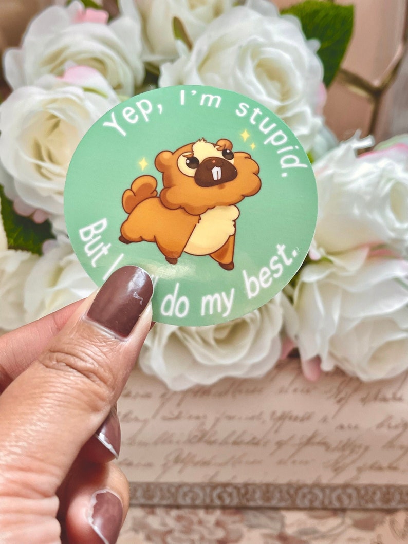 Puede incluir: Una pegatina redonda con una ilustraci&oacute;n de castor de dibujos animados en tonos marr&oacute;n y crema, sobre un fondo verde claro. La pegatina tiene el texto "Yep, I'm stupid. But I do my best." en blanco. La pegatina se sostiene en una mano.