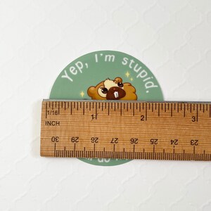 Puede incluir: Una pegatina redonda con un castor de dibujos animados y el texto "Yep, I'm stupid". La pegatina mide aproximadamente 5 cm de di&aacute;metro. El castor es marr&oacute;n y beige con un diente blanco y acentos brillantes.