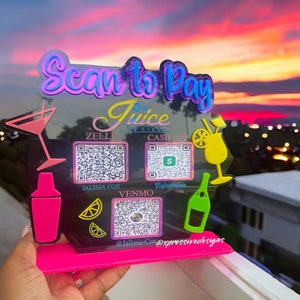 May include: A pink acrylic sign with the text "Scan to Pay Juice by Liss" and QR codes for Zelli, Cash App, Venmo, and Jalissa Cox. The sign is decorated with colorful cocktail glasses and lemons.