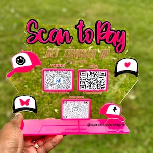 May include: A pink acrylic sign with the words "Scan to Pay" in a bubble font. The sign includes QR codes for Venmo, Etsy, and Instagram, along with decorative baseball caps.