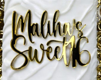 Puede incluir: Un adorno para pastel dorado con las palabras "Maliha's Sweet 16" en una fuente cursiva. El adorno está colocado sobre un pastel glaseado blanco. El fondo incluye elementos decorativos dorados.