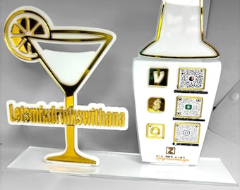 May include: Gold-colored acrylic cutout of a martini glass with a lemon slice and the text "Let's mix drinks with Thana".  A gold-colored acrylic cutout of a cocktail shaker with QR codes and social media icons.  The text "@ExpressiveDesigns" is also included.