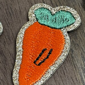 May include: A sparkly orange carrot with a green leafy top. The carrot has a black embroidered line down the center.