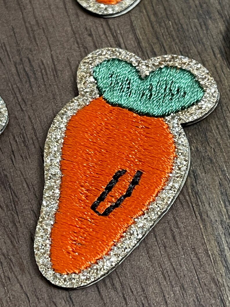 May include: A sparkly orange carrot with a green leafy top. The carrot has a black embroidered line down the center.