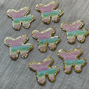 Op de afbeelding: Zeven kleurrijke vliegtuigvormige patches met een gouden glitterrand. De patches zijn gemaakt van stof en hebben een gestreept patroon in roze, groen en blauw.
