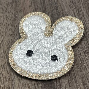 May include: White felt bunny head with gold glitter trim and black embroidered eyes.