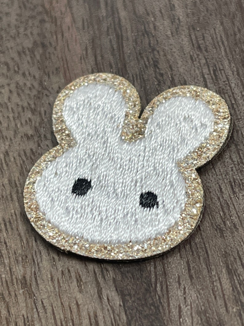 May include: White felt bunny head with gold glitter trim and black embroidered eyes.