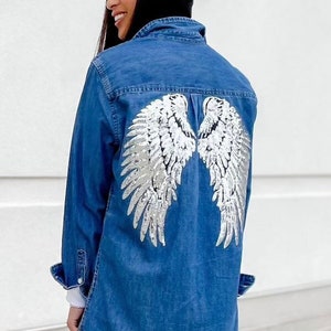 Puede incluir: Una chaqueta vaquera azul con alas de ángel de lentejuelas plateadas en la espalda.