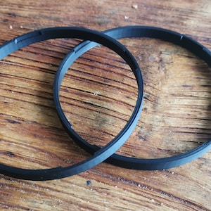 Könnte beinhalten: Zwei schwarze Gummringe, wahrscheinlich für ein Kameraobjektiv, liegen auf einer Holzoberfläche.