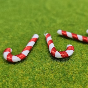 Puede incluir: Tres adornos de bastón de caramelo rojo y blanco sobre una superficie verde.