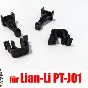 Könnte beinhalten: Vier schwarze Kunststoffclips für Computerkomponenten, darunter zwei mit einem Halterungsdesign und zwei mit einem gebogenen Design. Der Text "Made in Germany" und "für Lian-Li PT-J01" sind ebenfalls sichtbar.