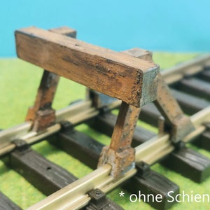 Könnte beinhalten: Ein hölzerner Bahnübergang mit einem braunen Holzbalken und zwei braunen Holzpfosten. Der Übergang ist auf einem Modellbahngleis platziert. Der Text *ohne Schiene* ist im Bild sichtbar.