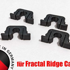 May include: Four black, C-shaped clips are shown against a white background. The number "4x" is in red in the upper left corner. The text "Made in Germany" and "für Fractal Ridge Case" are also visible.